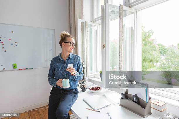 Coffee Break Woman Sitting On The Desk Using Smart Phone Stock Photo - Download Image Now