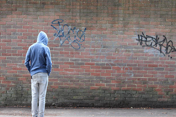 Image of teenage boy / youth wearing hoodie, beside graffiti wall Photo showing a teenage boy / youth wearing a blue hoodie and standing beside a brick wall, in a run-down part of the city. child crimes stock pictures, royalty-free photos & images