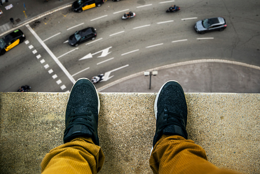 Two feet at the edge of a rooftop of a high building. A busy street appears looking down.