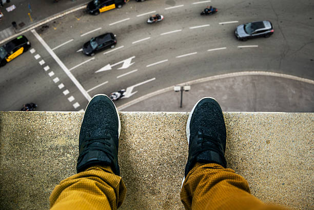 Suicide about to jump Two feet at the edge of a rooftop of a high building. A busy street appears looking down. personal perspective standing stock pictures, royalty-free photos & images