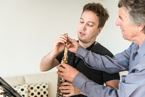 Young man learning how to play saxophone at home, teacher showing how to play instrument with finger