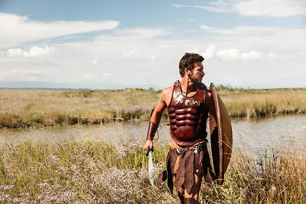 Portrait of fighting ancient warrior in armor with sword and shield.  Spartan Soldier. Landscape background