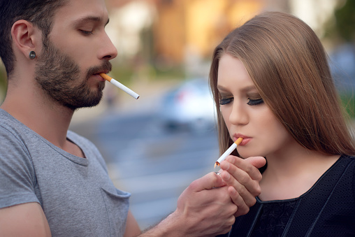 portraits of cool couple lighting up cigarettes, having attitudes and posing in urban scene.head and shoulders.