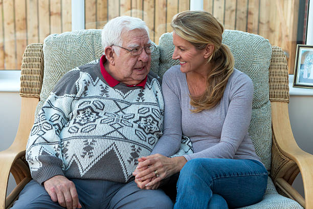 Daughter Visiting Her Senior Father An adult daughter is sat holding her senior farther hand and chatting to one another and smiling. father daughter 80s stock pictures, royalty-free photos & images