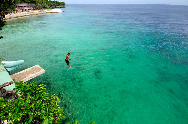 Dive into Siquijor Siquijor, Philippines April 5th, 2015: A boy jumps off a cliff into ocean waters.   siquijor island stock pictures, royalty-free photos & images