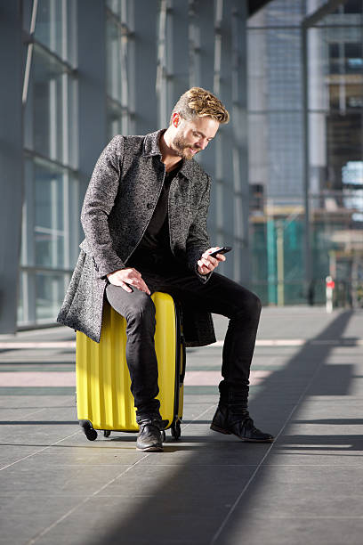 istock Cool travel guy sitting on suitcase looking at mobile phone 504878986