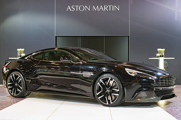 Brussels, Belgium - Januari 12, 2016: Black Aston Martin Vanquish sports car front view. The car is on display during the 2016 Brussels Motor Show. The car is displayed on a motor show stand, with lights reflecting off of the body. There are people looking around and other cars on display in the background.