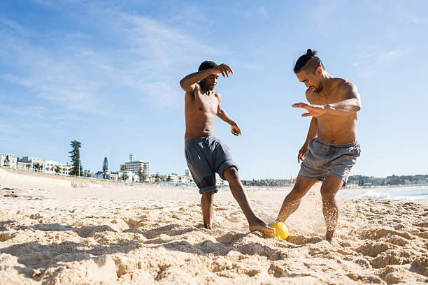 hombres guapos jugando al fútbol en la playa - beach football fotografías e imágenes de stock