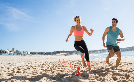 Happy young couple exercising outdoors at the beach in Australia running on the sand with obstacles