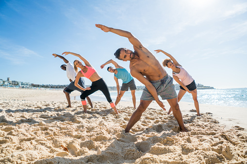 Group of young people in an aerobics class at the beach - fitness concepts
