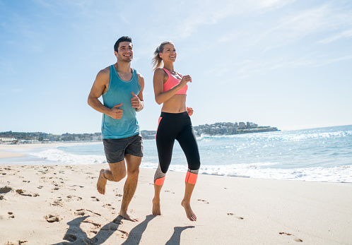 Fit couple running barefoot at the beach and looking happy exercising - healthy lifestyle concepts