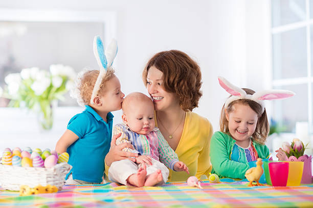 Mother with three children painting Easter eggs Mother and children painting colorful eggs. Mom, toddler, preschooler and baby with bunny ears paint and decorate Easter egg. Parent and kids play indoors in spring. Family celebrating Easter at home. holding child flower april stock pictures, royalty-free photos & images