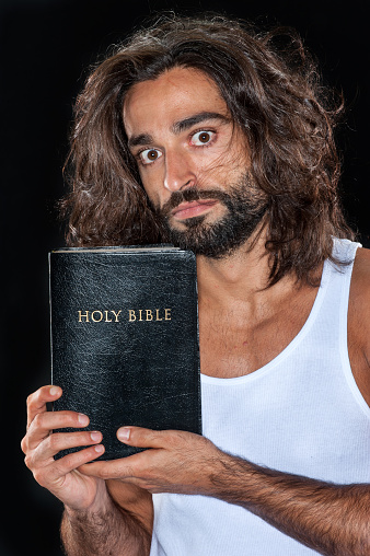 Bearded mid adult man holding his bible looking at the camera on black background