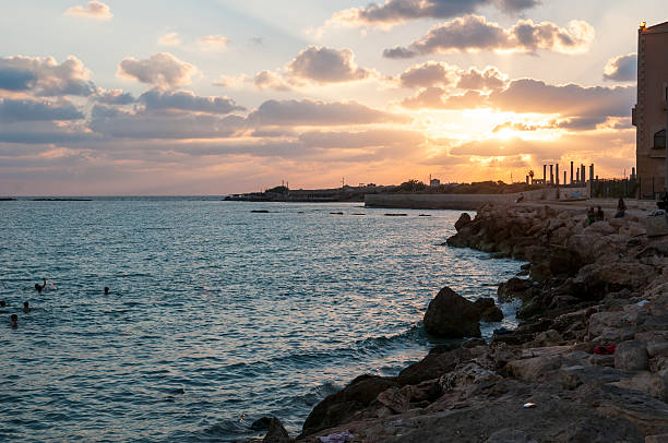 Tyre, Lebanon - August 31, 2010: People swim in the Mediterranean Sea as the sun sets behind ancient columns at Al-Mina Archaeological Site in Tyre, Lebanon.