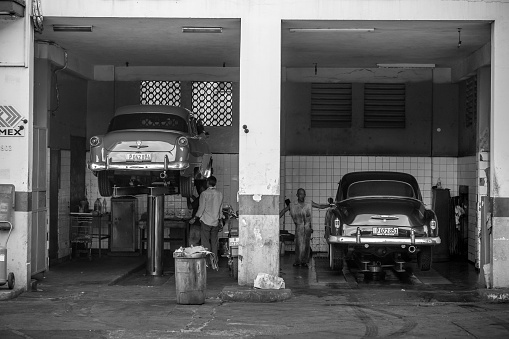 Havana, Cuba - November 6, 2015. Classic Havana Public Car wash. 43. Avenue in Miramar, suburbs of Havana city. This old fashion car wash is part of the public (government run) location where Havana drivers can come and detail their cars. In one bay,  Two man at the back of garage behind  of classic American car lifted. In another bay, Older Cuban man washing the rear end of classic American car lifted in the garage. Two of countless vintage US made cars imported to Cuba before the Revolution but still running after more than 50 years due to ingenuity of Cuban car mechanics and some help of various old car parts, including the left over of Russian diesel engines.   