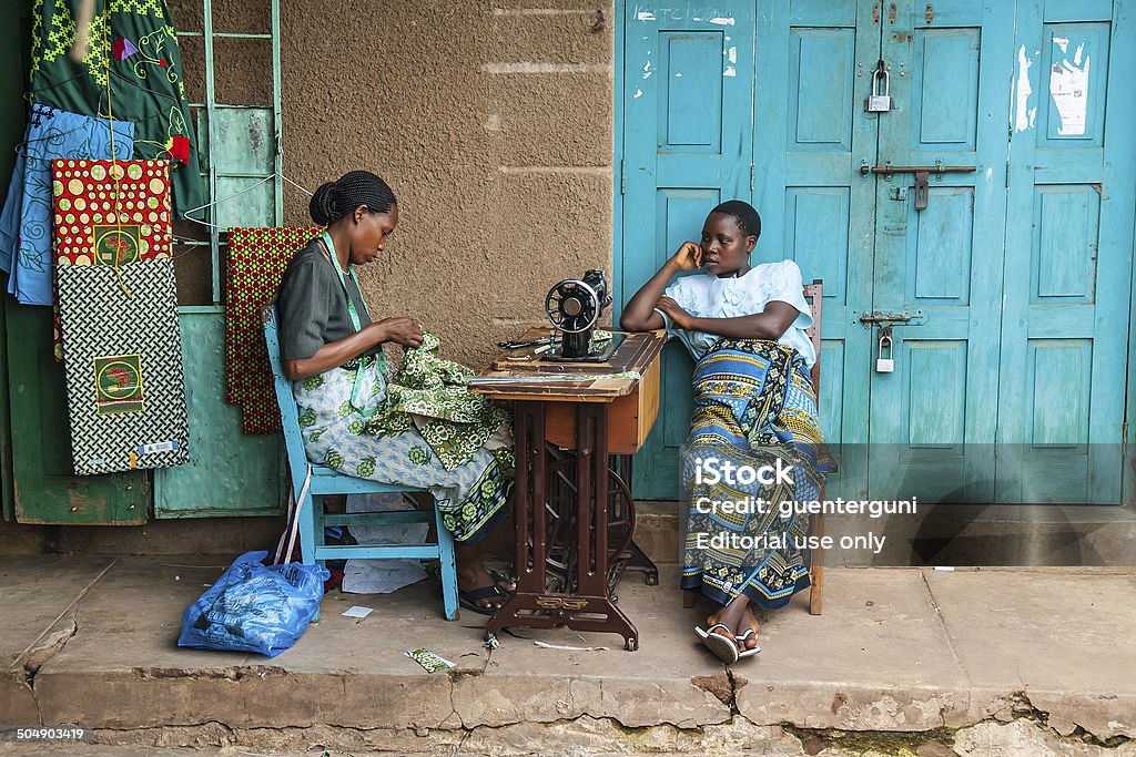 Two African woman sitting next to sewing machine Kigoma, Tanzania - December 29, 2009: Two African woman sitting next to sewing machine, in the background there is some fabcric hanging on the wall They are running their business outdoor on the streets of tKigoma town at Lake Tanganyika. Business Stock Photo