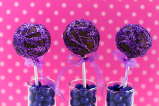 Purple swirled chocolate cake pops with light pink polka dot background standing in candy filled shot glasses