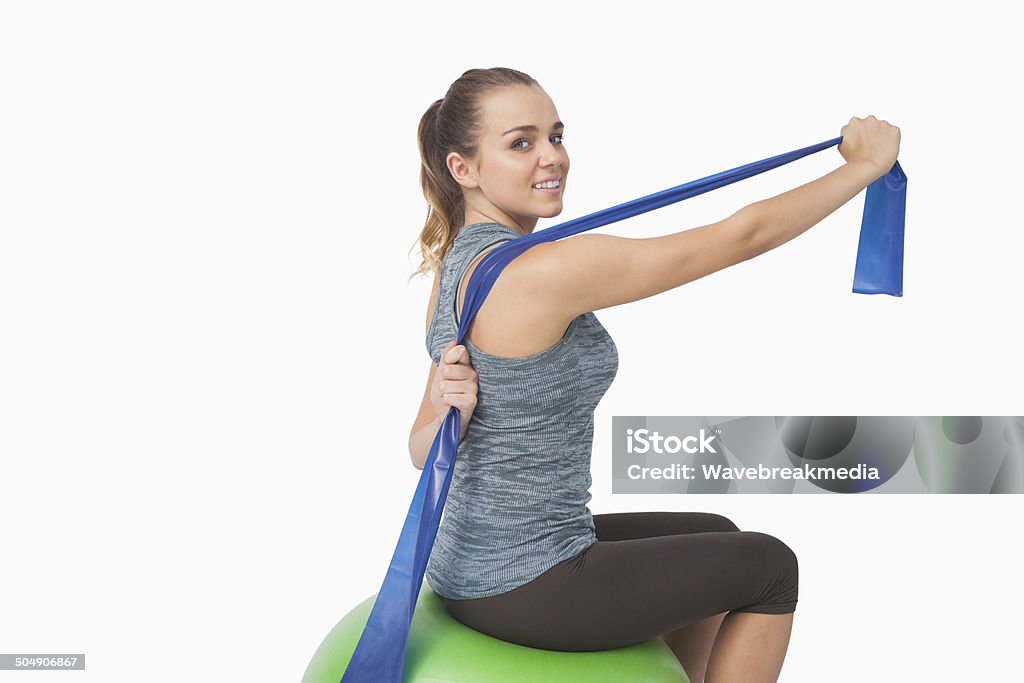 Pretty fit woman stretching her arms with a resistance band Pretty fit woman stretching her arms with a resistance band sitting on a fitness ball Adult Stock Photo