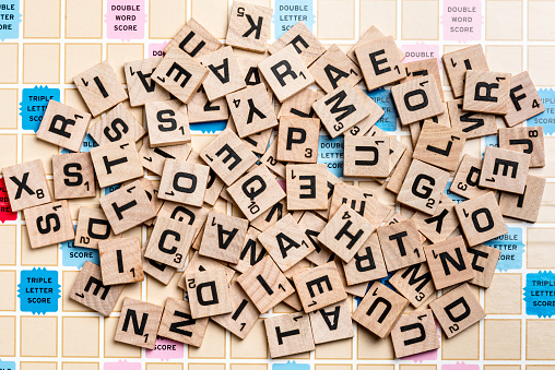 Miami, Florida, USA - May 25, 2015: Lettered wooden tiles mixed up on Scrabble game board. Scrabble is a fun and educational game distributed by Hasbro