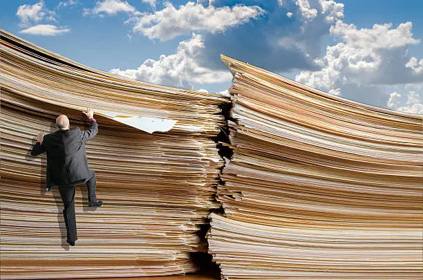 Business man climbing up a pile of files to reach the top, with sky as background