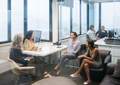 Women sitting on chairs with female manager at desk, in meeting. Female colleagues discussing work, serious conversation between multiracial businesswomen.