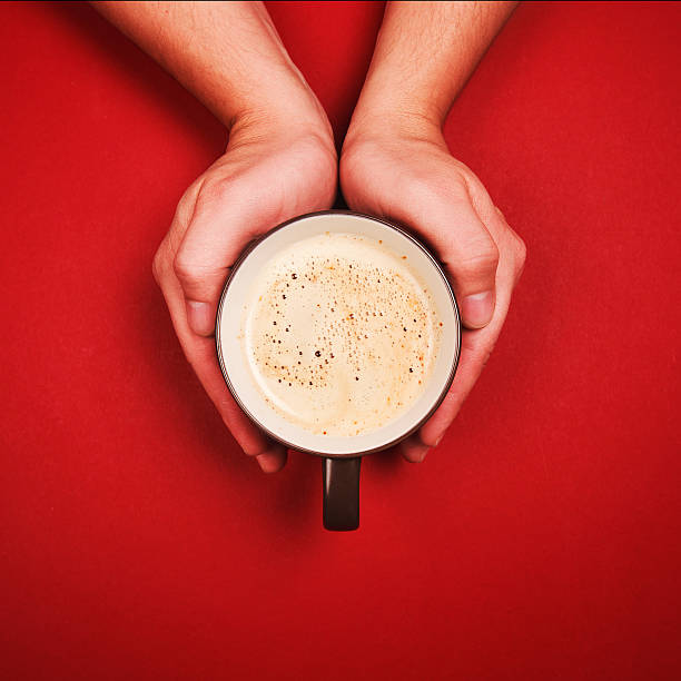 Two hands holding a cup of fresh coffee with foam on red background