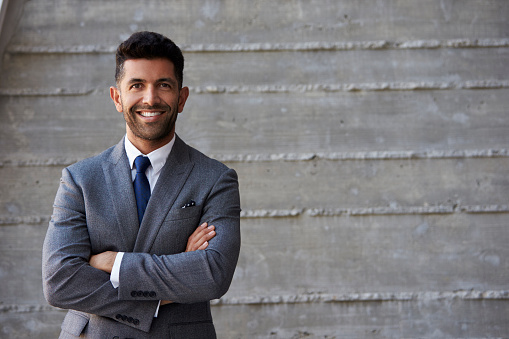 Hispanic Businessman Standing Against Wall In Modern Office