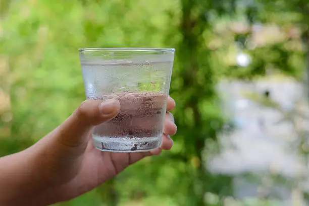 Glass water,Ice glass in hand,green blur background.focus glass top.