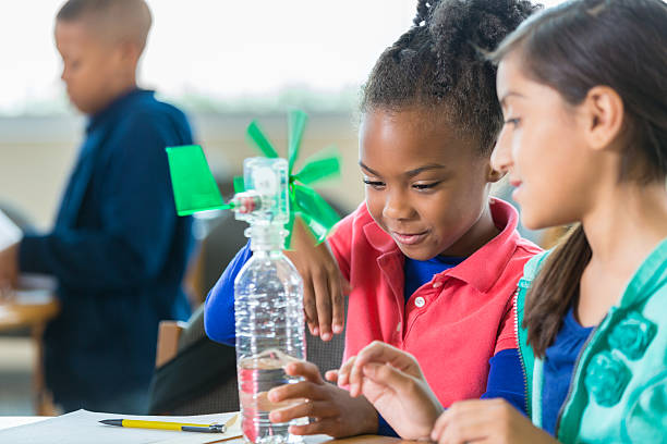 Students building windmill during elementary science class African American and Hispanic elementary age little girls are building a windmill from a water bottle during an after school science program in a public elementary school library. Students are learning science, technology, engineering, and math while working on science project together. science class stock pictures, royalty-free photos & images