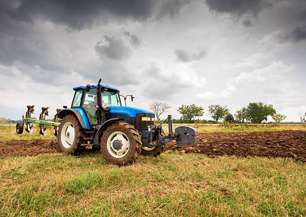 trattore e drammatico cielo blu - hay wheat bale stacking foto e immagini stock