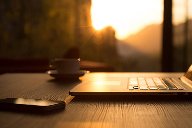 istock Computer Coffee Mug Telephone on black wood table sun rising 505032744