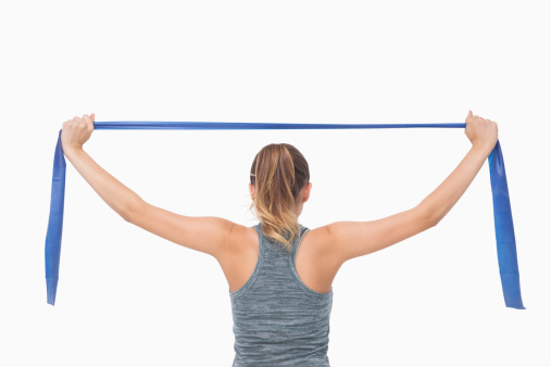 Ponytailed woman training with a resistance band on white background