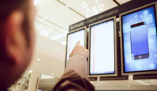 Dubai, United Arab Emirates - January 13, 2016: Man traveling through an airport and pointing his hand towards an airport arrival display panel. Dubai International Airport is the primary airport serving Dubai, United Arab Emirates and is one of the world's busiest airport by international passenger traffic. It is also the 3rd busiest airport in the world by passenger traffic, the 6th busiest cargo airport in world and the busiest hub for the Airbus A380. In 2014, DXB handled 70.5 million passengers, 2.37 million tonnes of cargo and registered 357,339 aircraft movements.