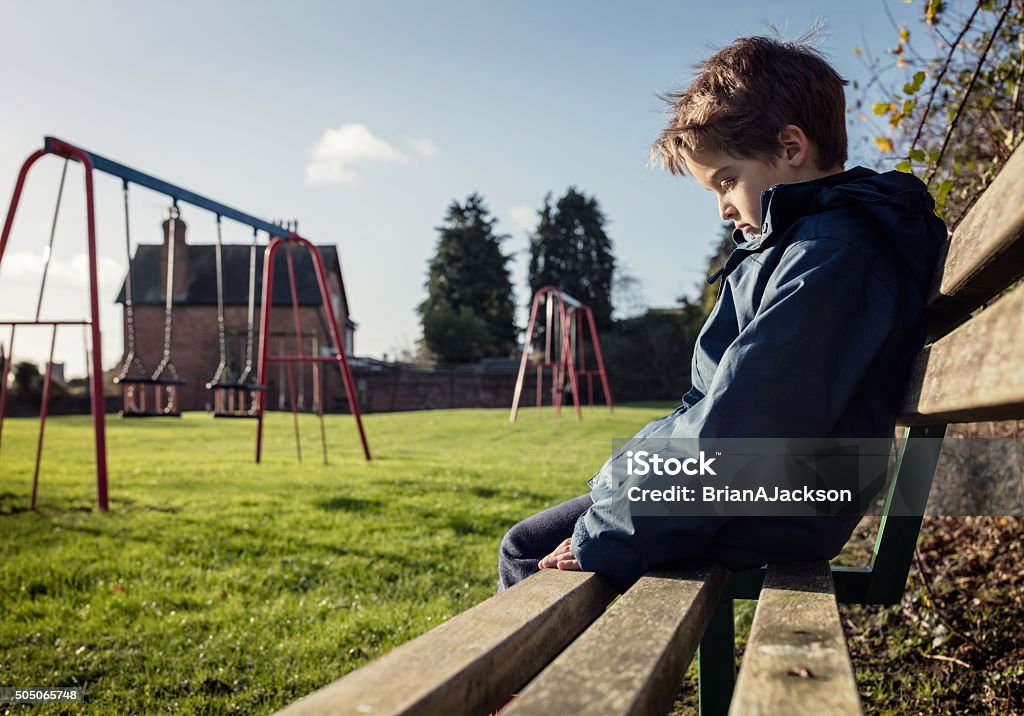 Lonely child sitting on play park playground bench Upset problem child sitting on play park playground bench concept for bullying, depression, child protection or loneliness Child Stock Photo
