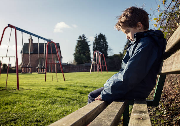 Lonely child sitting on play park playground bench Upset problem child sitting on play park playground bench concept for bullying, depression, child protection or loneliness child crimes stock pictures, royalty-free photos & images