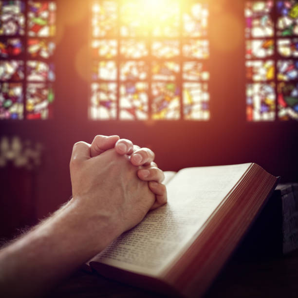 Hands folded in prayer on a Holy Bible in church concept for faith, spirtuality and religion