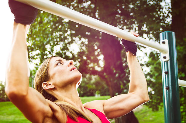 Athletic Woman Doing Pull-Ups On a Sunny Day Experienced athlete is doing pull-ups, outdoor setting. chin ups photos stock pictures, royalty-free photos & images