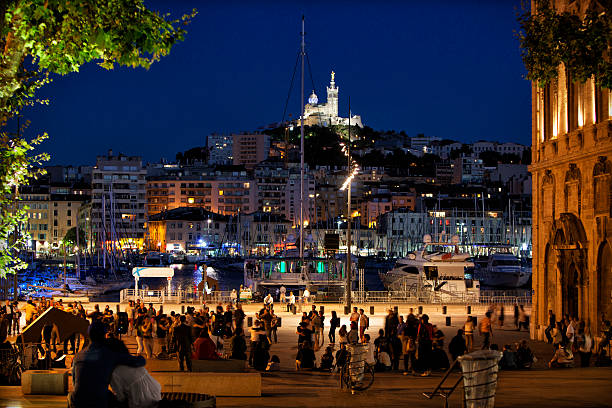 Night scene with motion blur of couples dancing Tango at the Vieux Port, Marseille, France. The Basilica was built on the highest point and is the most famous landmark of the city.