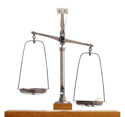 Vintage metal scale with the two pans out of equilibrium with one lower than the other isolated on white, conceptual of measurement, inequality and justice