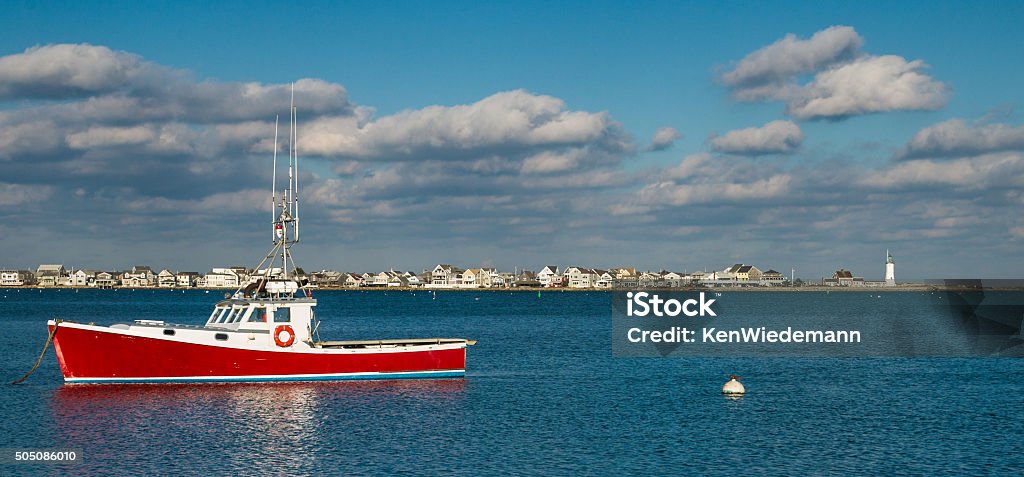 Lobster Boat off Scituate Light. A red lobster boat is moored off Cedar Point in Scituate, Massachusetts on a cold January afternoon. Scituate Lighthouse is seen in the distance. Community Stock Photo