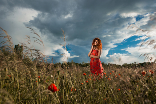 Red haired woman in a field at sunset and wearing in red dress