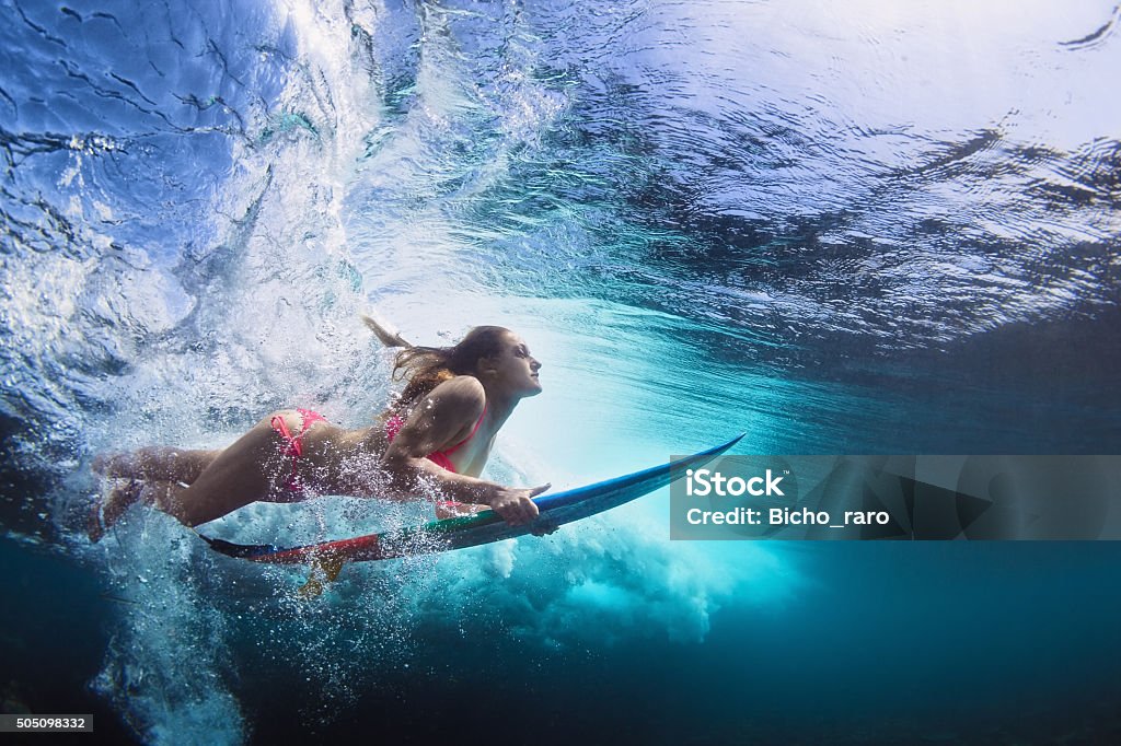 Underwater photo of girl with board dive under ocean wave Young girl in bikini - surfer with surf board dive underwater with fun under big ocean wave. Family lifestyle, people water sport lessons and beach swimming activity on summer vacation with child Surfing Stock Photo