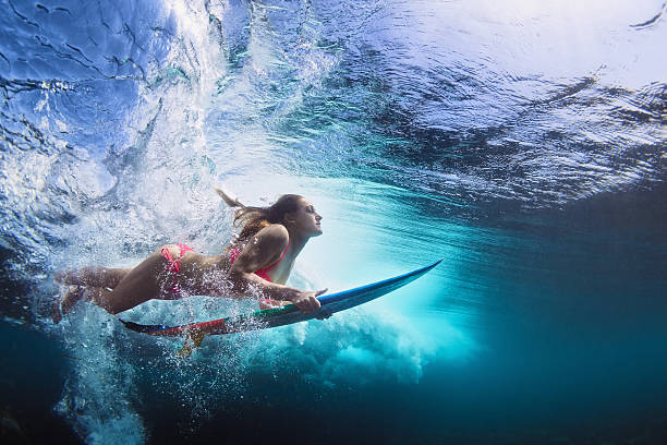 Underwater photo of girl with board dive under ocean wave Young girl in bikini - surfer with surf board dive underwater with fun under big ocean wave. Family lifestyle, people water sport lessons and beach swimming activity on summer vacation with child diving into water photos stock pictures, royalty-free photos & images