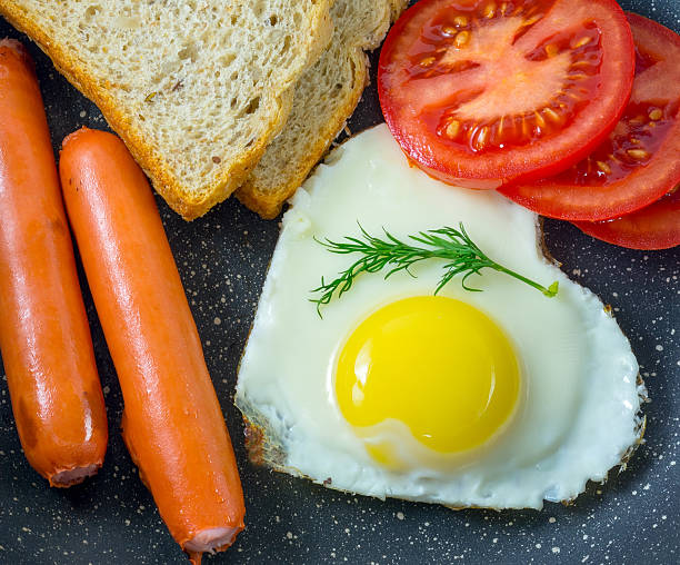 Breakfast fried egg in heart-shaped, grilled sausages, bread