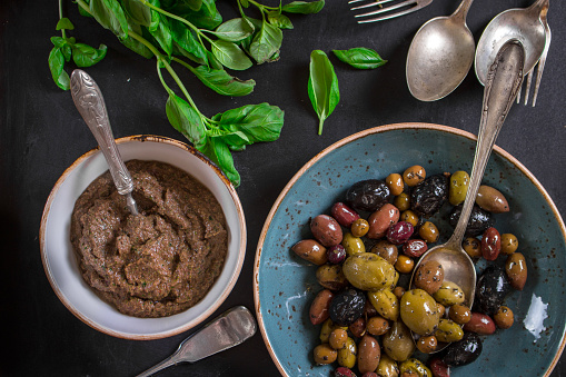 Table served with tapenade, mixed marinated olives (green, black and purple) in ceramic bowl and basil leaves. French provence appetizers and snacks. Close-up