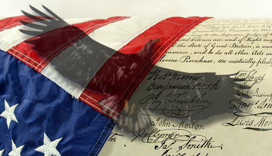Close-up of some of the  signatures on the Declaration of Independence with a  transparent image of an eagle over the image and the USA  flag.