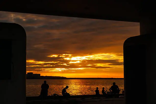 People fishing from a pier on the Lake Erie shore of Cleveland and silhouetted by the setting sun