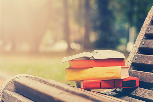 Stack of hardback books and Open book lying on bench at sunset park against blurred nature backdrop. Copy space, back to school. Education background. Toned image.