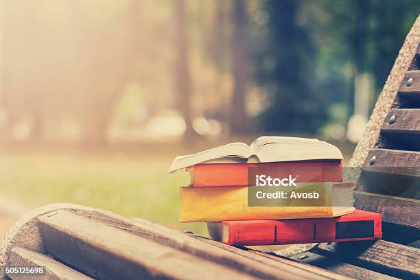 Stack Of Hardback Books And Open Book Lying On Bench Stock Photo - Download Image Now
