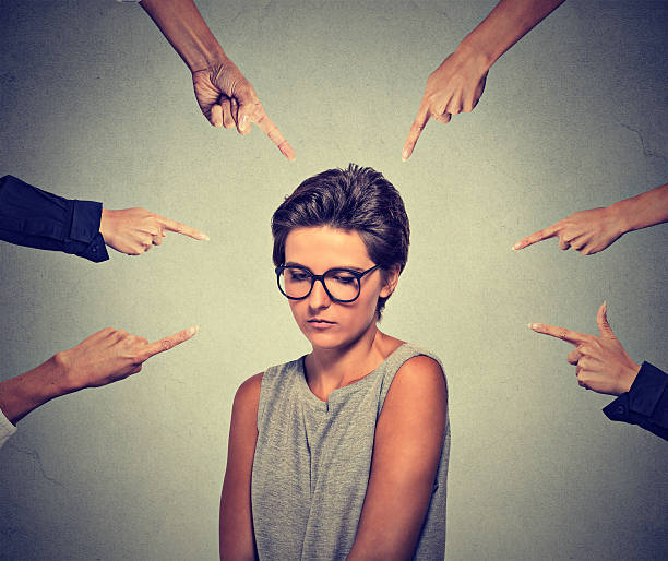 Embarrassed woman looking down many fingers pointing at her Concept of accusation guilty shy person girl. Sad embarrassed upset woman in glasses looking down many fingers pointing at her isolated grey wall background. Human face expression emotion feeling stereotypical stock pictures, royalty-free photos & images